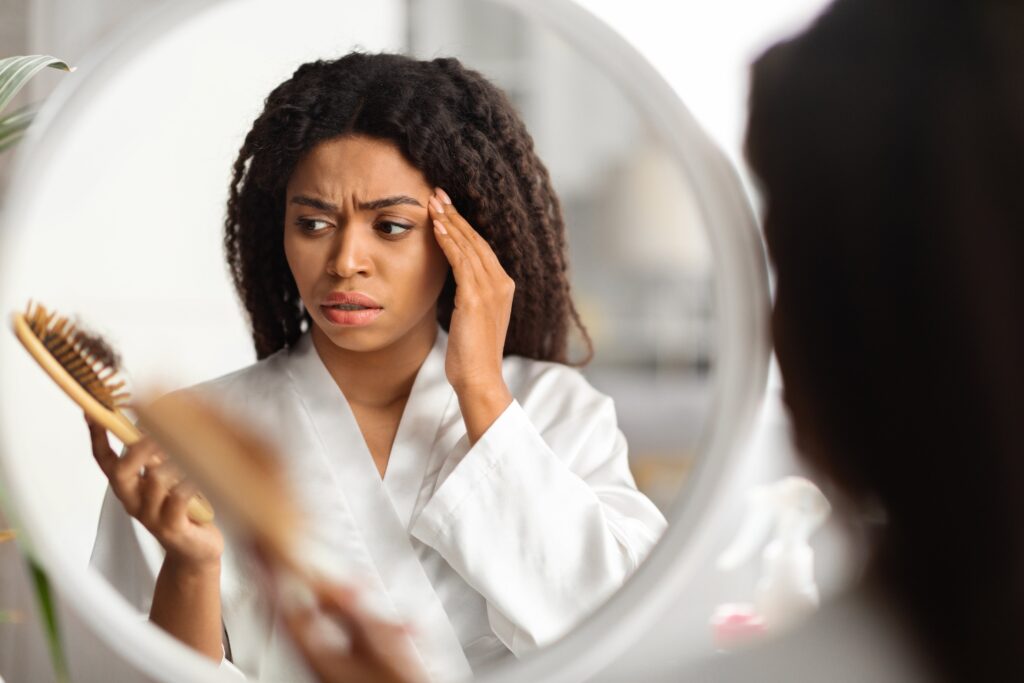 Femme noire victime de perte de cheveux, tenant un peigne avec de nombreux cheveux perdus