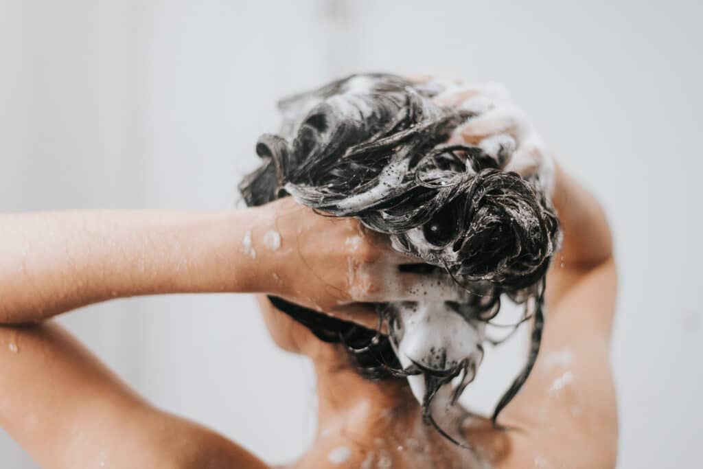 Vrouw wast haar met shampoo en douche in badkamer