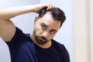 Man wondering why do hair transplants fail? while looking at thin hair in the mirror